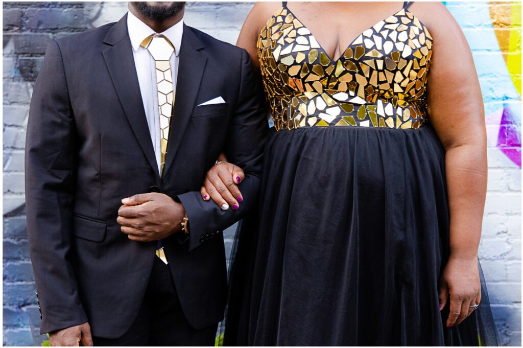 A close up of the torso of the couple, the man in a suit ion the left and the woman in a gold and black dress on the right. 